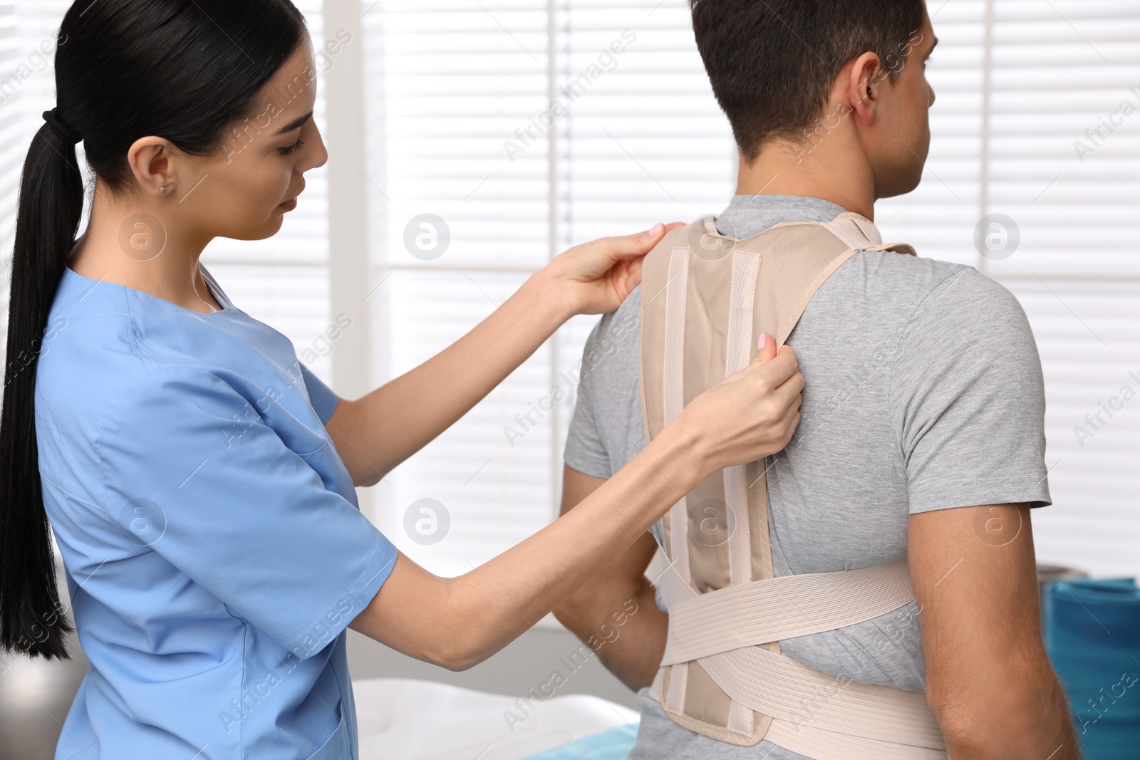 Photo of Orthopedist helping patient to put on posture corrector in clinic. Scoliosis treatment