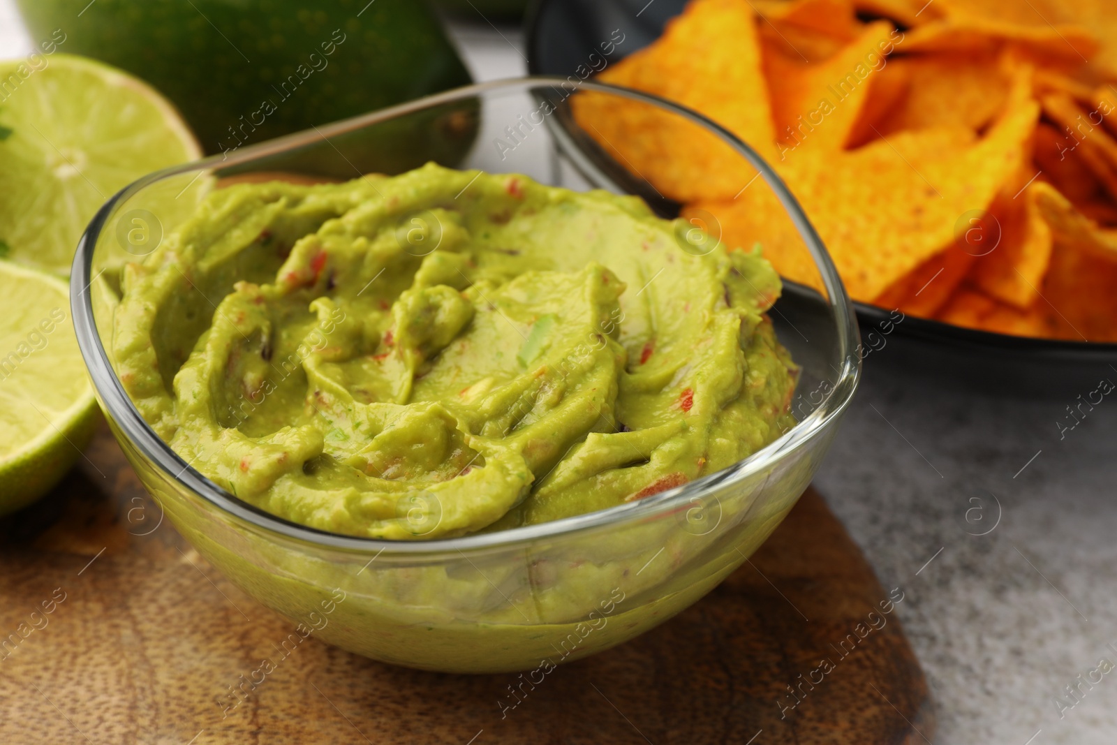Photo of Bowl of delicious guacamole served with nachos chips and lime on table, closeup