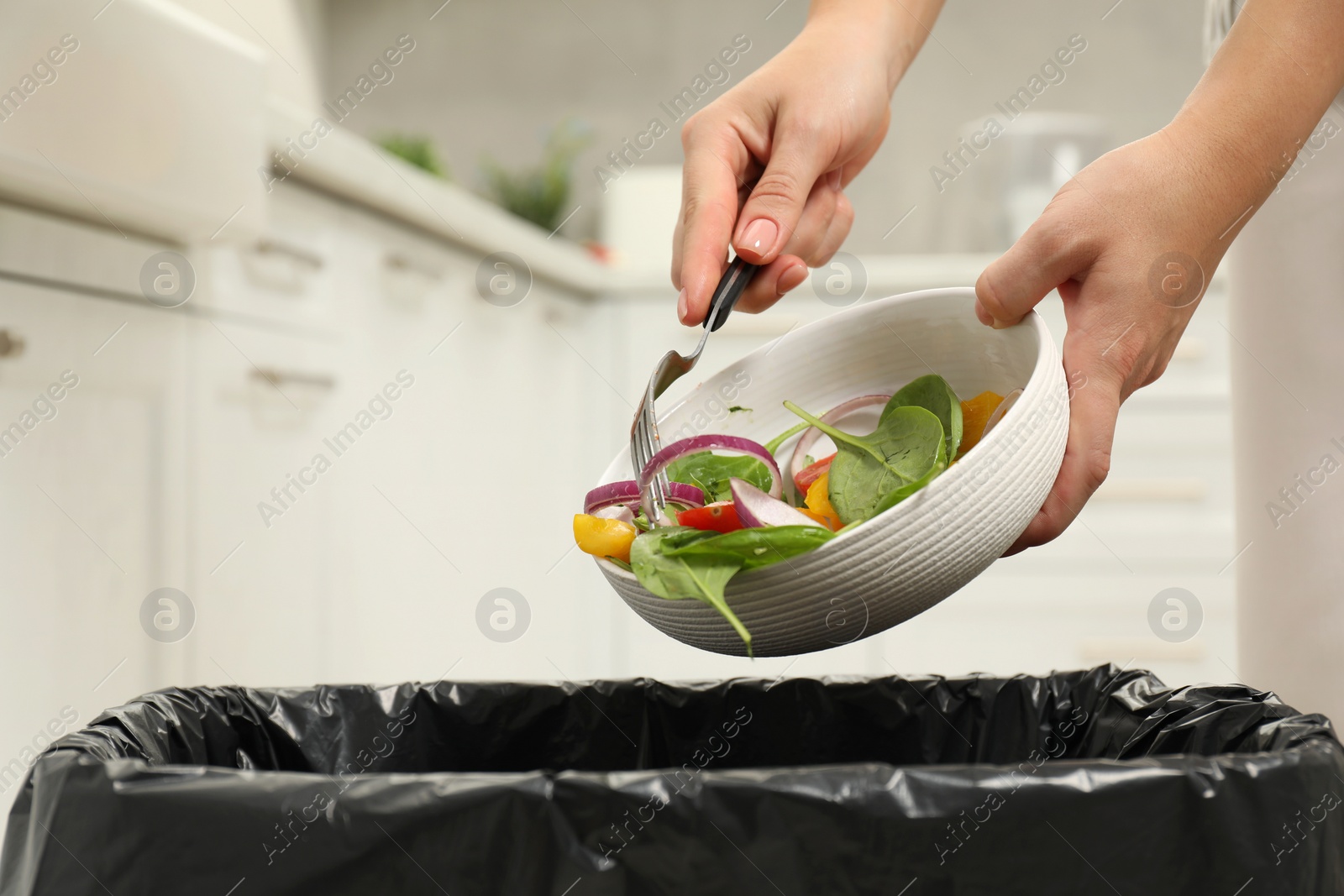 Photo of Woman throwing vegetable salad into bin indoors, closeup