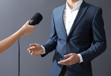 Photo of Professional journalist interviewing businessman on grey background, closeup