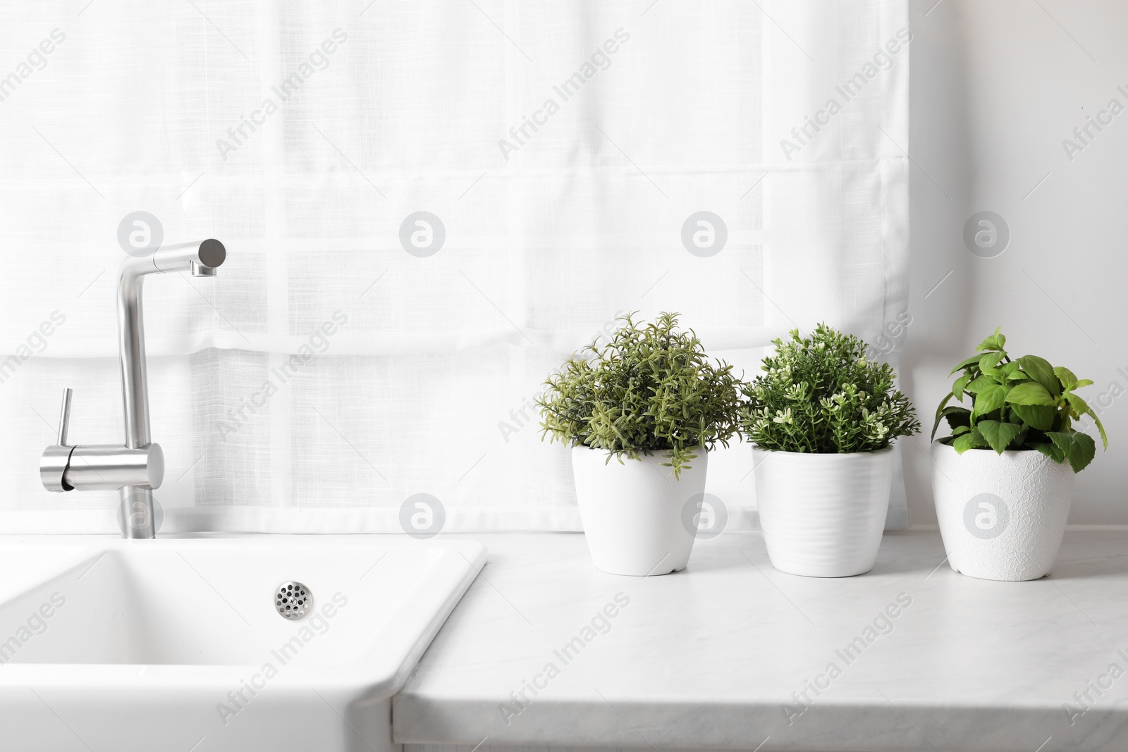 Photo of Artificial potted herbs on white marble countertop near sink in kitchen. Home decor