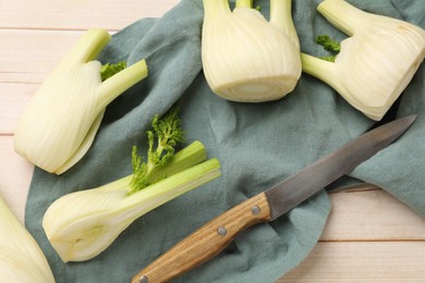 Fresh raw fennel bulbs and knife on light wooden table, flat lay