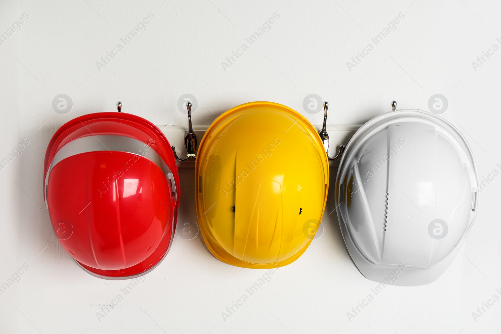 Photo of Hard hats hanging on white wall. Safety equipment