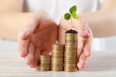 Photo of Woman with stack of coins and green sprout at white table, closeup. Investment concept