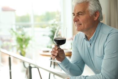 Senior man with glass of wine in restaurant. Space for text