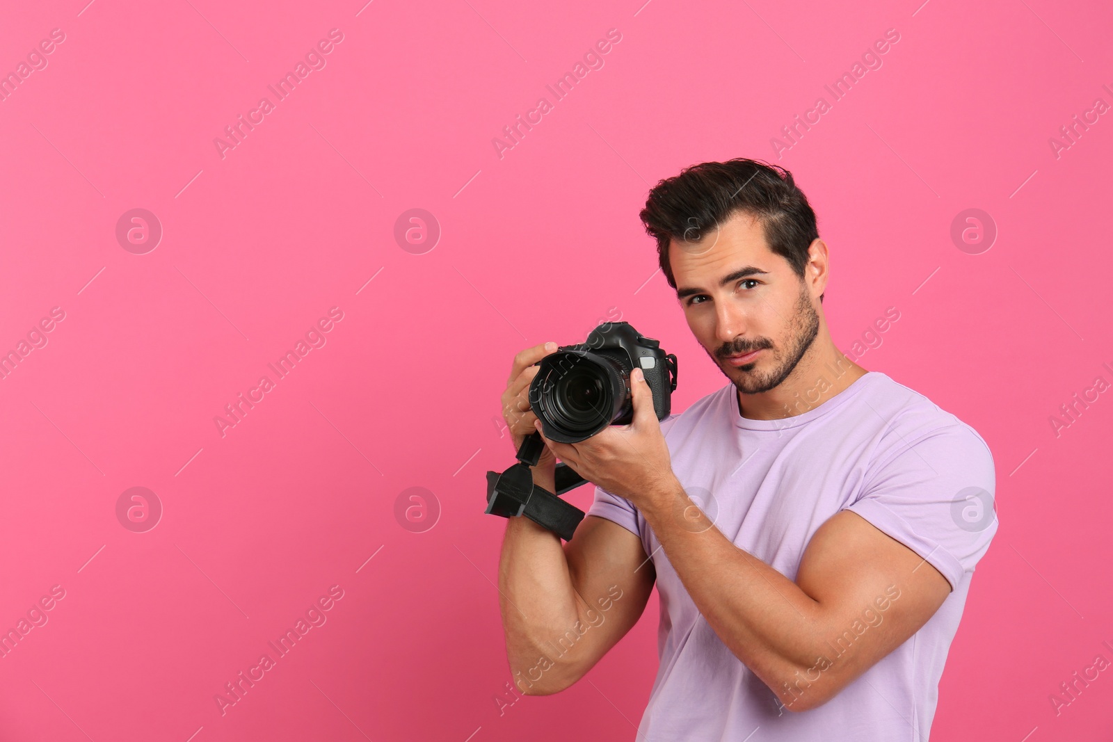 Photo of Young photographer with professional camera on pink background. Space for text