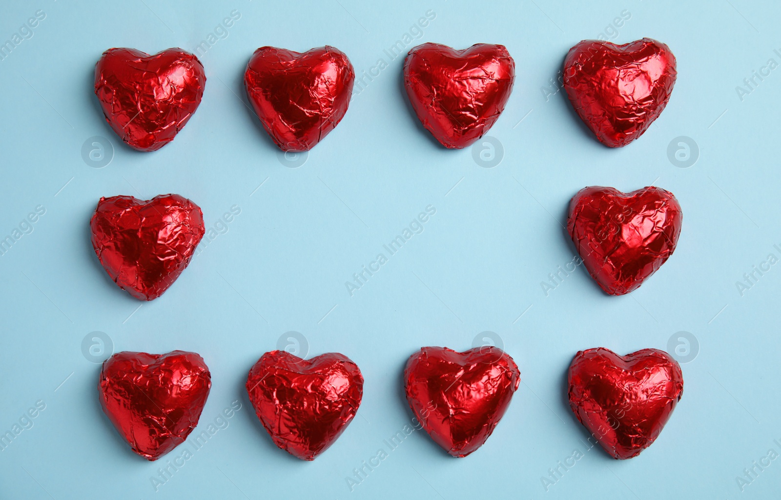 Photo of Frame of heart shaped chocolate candies on light blue background, flat lay with space for text. Valentine's day treat