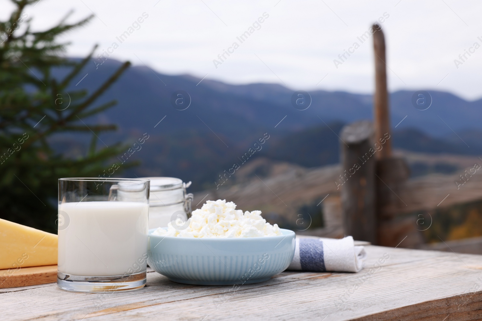 Photo of Tasty cottage cheese and other fresh dairy products on wooden table in mountains