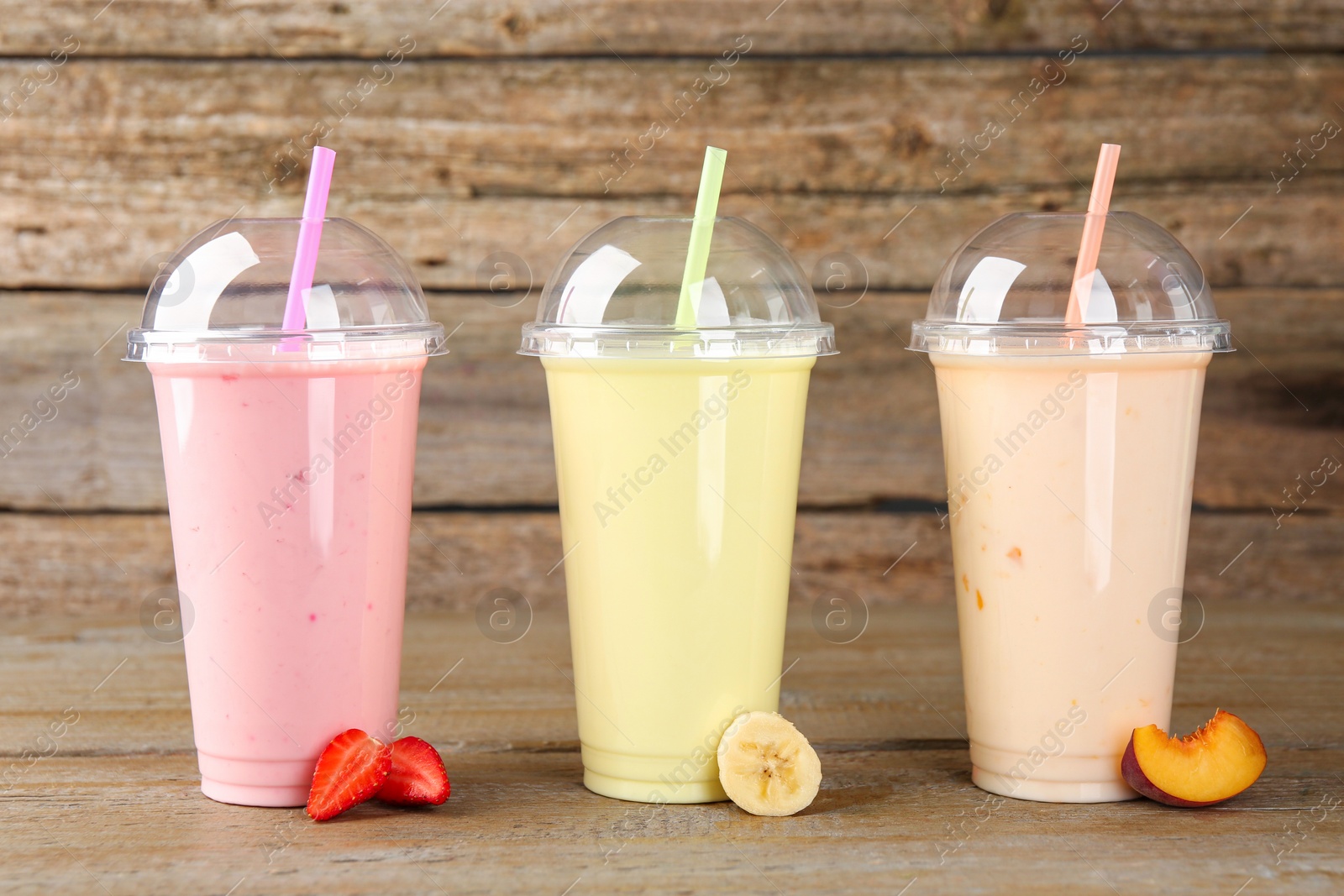 Photo of Plastic cups with different tasty smoothies and fresh fruits on wooden table