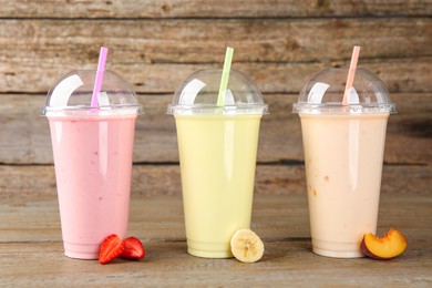 Photo of Plastic cups with different tasty smoothies and fresh fruits on wooden table