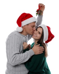 Photo of Happy man kissing his girlfriend under mistletoe bunch on white background