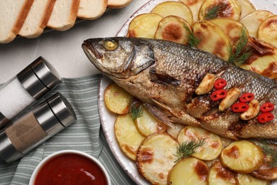 Plate with delicious baked sea bass fish and potatoes on table, flat lay