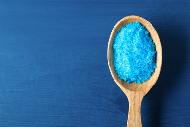 Photo of Spoon with sea salt on blue wooden table, top view. Space for text