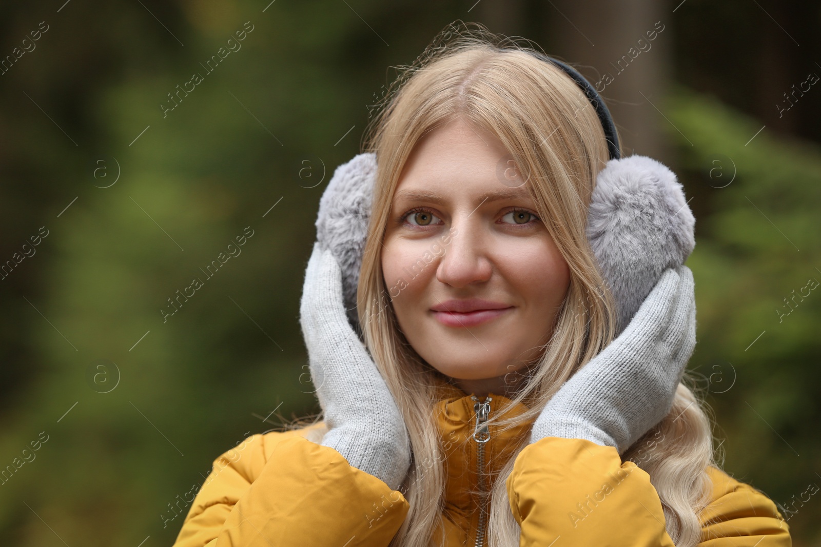 Photo of Young beautiful woman wearing warm earmuffs outdoors