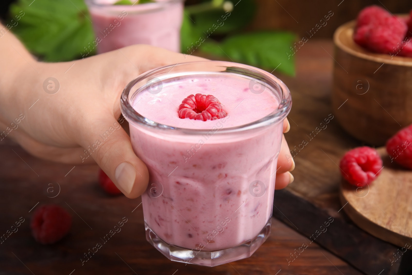 Photo of Woman holding glass of tasty raspberry smoothie over wooden table, closeup