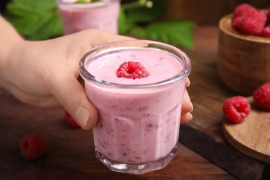 Woman holding glass of tasty raspberry smoothie over wooden table, closeup