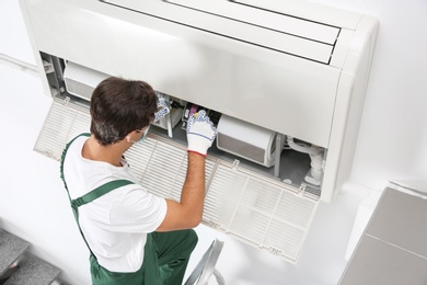 Photo of Young male technician repairing air conditioner indoors