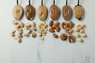 Photo of Tasty nut butters in spoons and raw nuts on white marble table, flat lay. Space for text