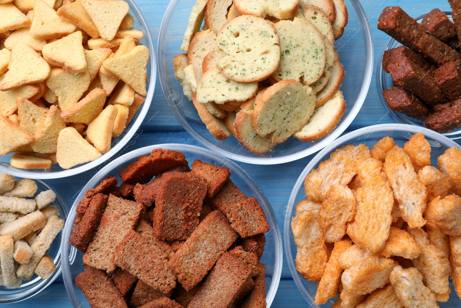 Photo of Different crispy rusks in bowls on light blue wooden table, flat lay