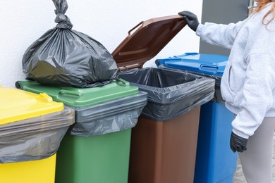 Photo of Woman opening bin to throw trash bag full of garbage outdoors, closeup. Recycling concept