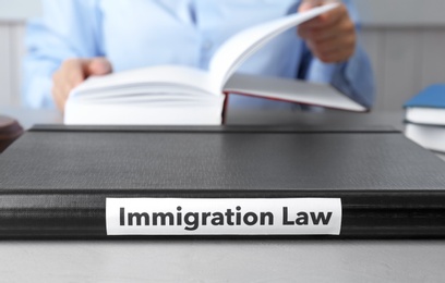 Photo of Folder with words IMMIGRATION LAW and blurred person on background