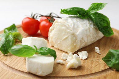 Photo of Delicious goat cheese with tomatoes and basil on wooden board, closeup