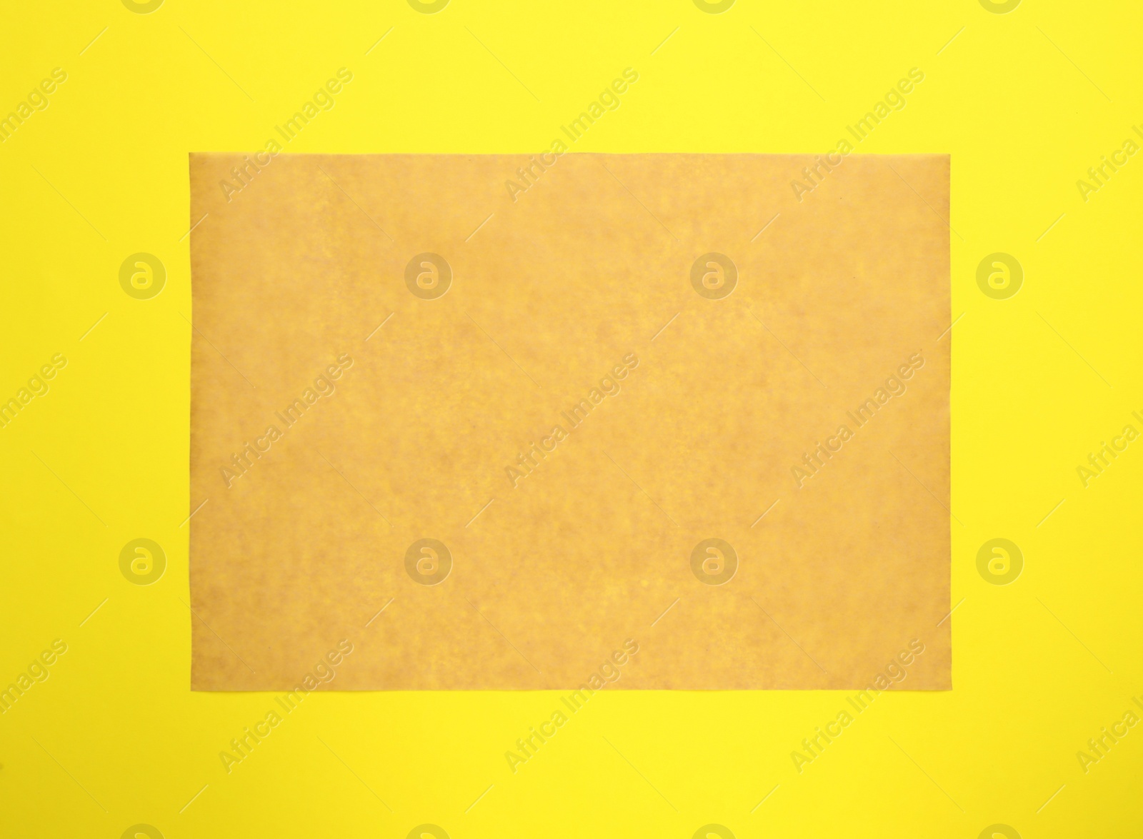 Photo of Sheet of brown baking paper on yellow background, top view