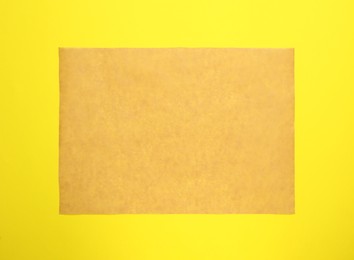 Sheet of brown baking paper on yellow background, top view
