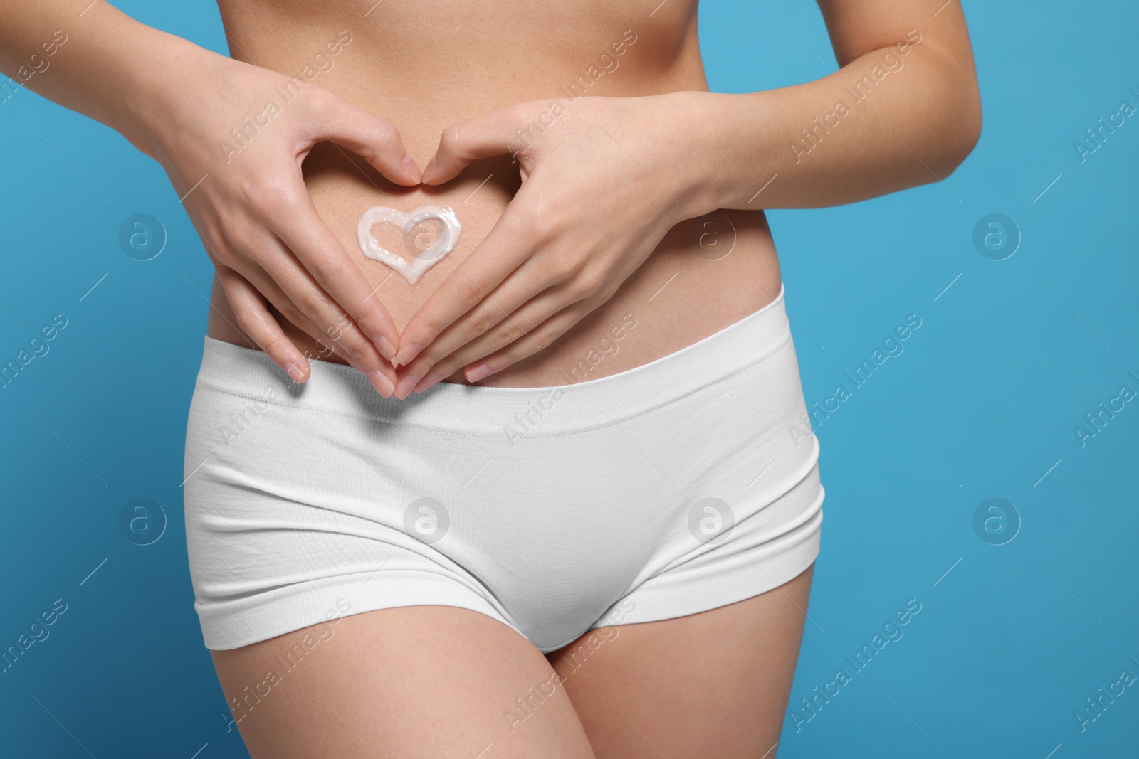 Photo of Woman with heart made of body cream on her belly against light blue background, closeup