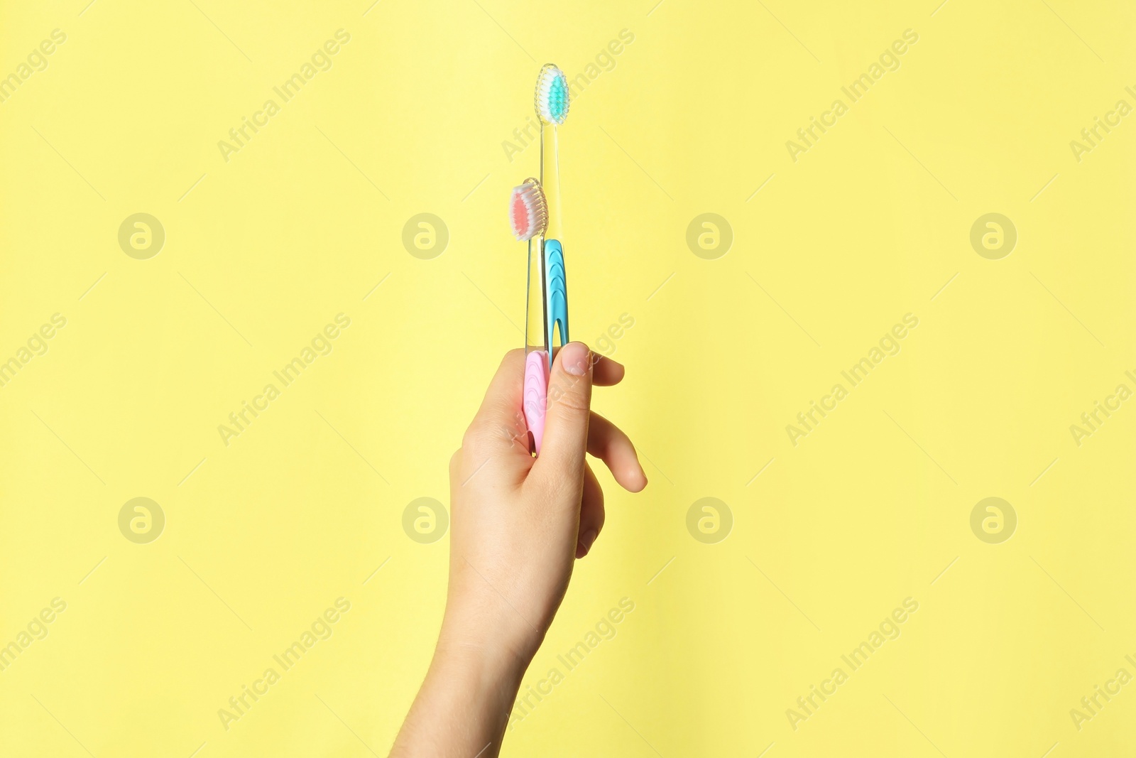 Photo of Woman holding manual toothbrushes against color background