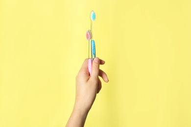 Woman holding manual toothbrushes against color background