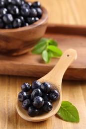 Photo of Spoon with tasty fresh bilberries on wooden table, closeup