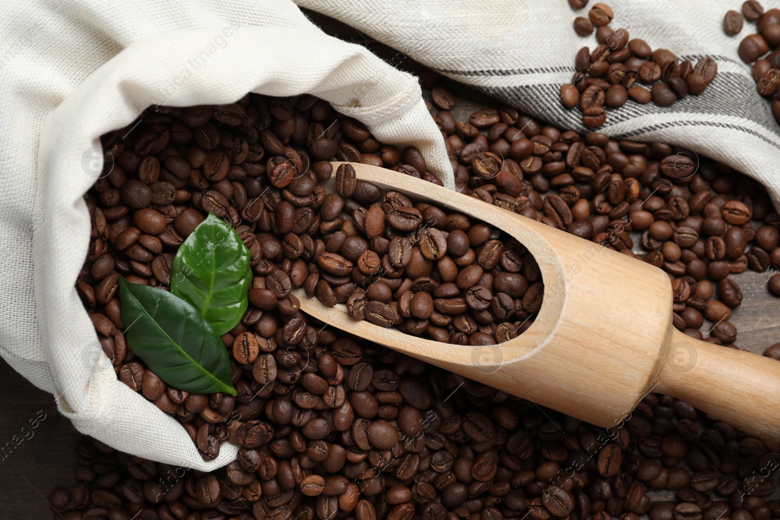 Photo of Scoop and bag with roasted coffee beans on wooden table, flat lay