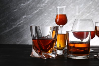 Different delicious liqueurs in glasses on dark wooden table