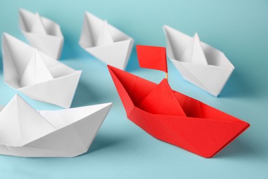 Photo of Red paper boat among others on light blue background. Uniqueness concept