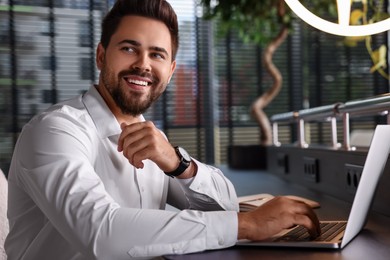 Happy young man working on laptop at table in office