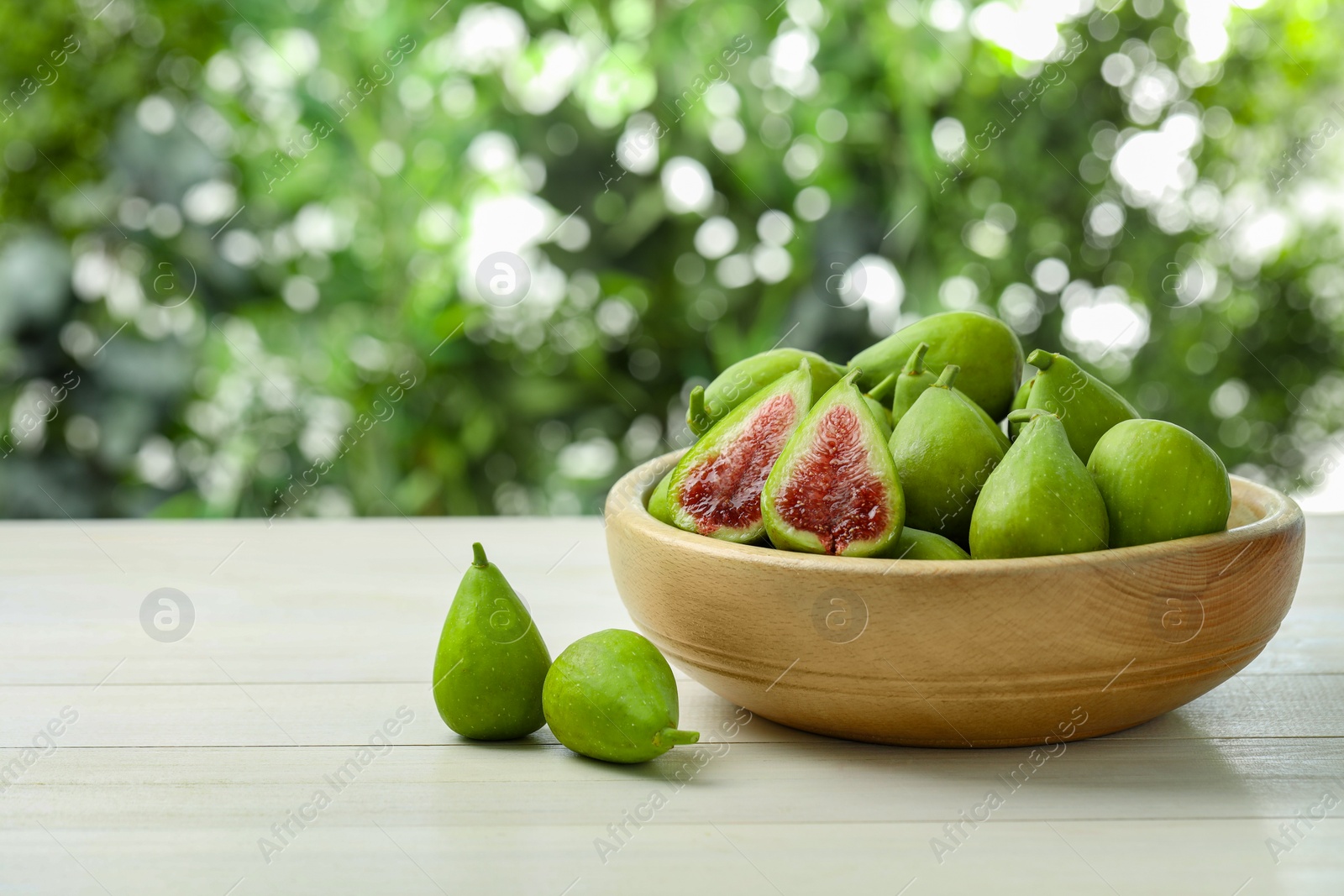 Photo of Cut and whole fresh green figs on white wooden table against blurred background, space for text