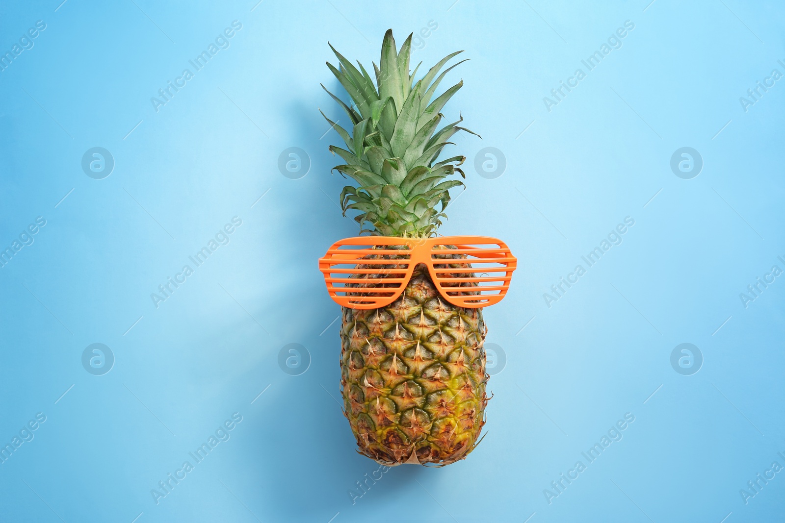 Photo of Fresh ripe pineapple with sunglasses on color background, top view