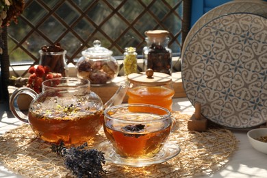 Photo of Aromatic tea with different dry plants and honey on white wooden table near window