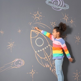 Photo of African-American child playing with chalk rocket drawing on grey background