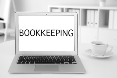 Image of Bookkeeping concept. Modern laptop and cup of coffee on white table in office