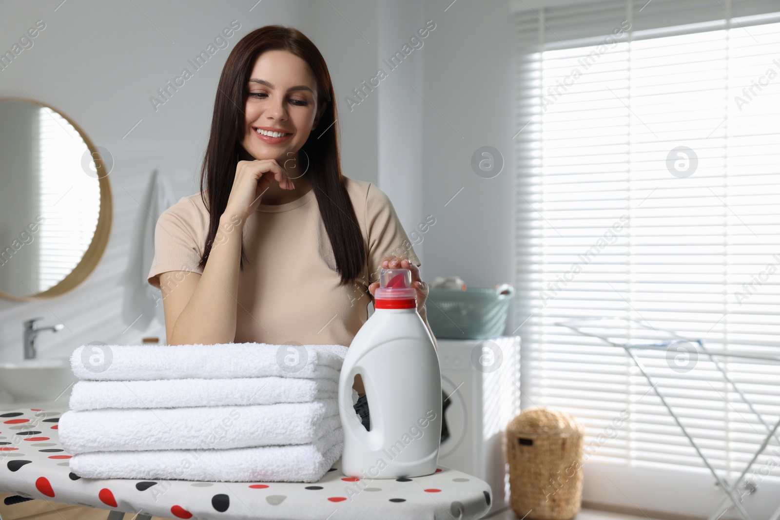Photo of Woman near fabric softener and clean towels in bathroom, space for text