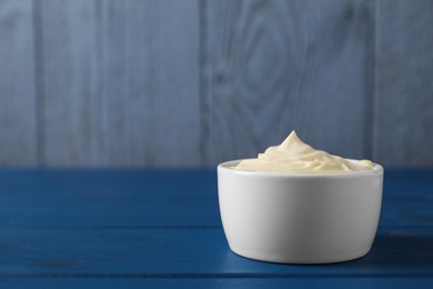 Photo of Tasty mayonnaise in bowl on blue wooden table, space for text