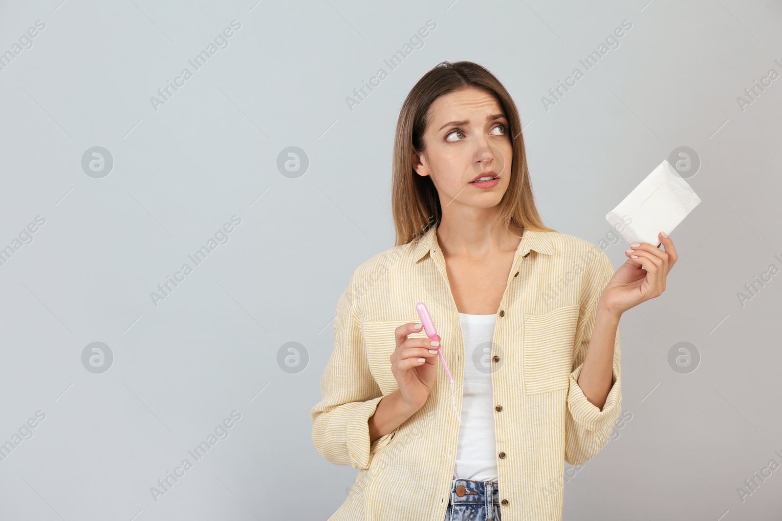 Photo of Thoughtful young woman with disposable menstrual pad and tampon on grey background