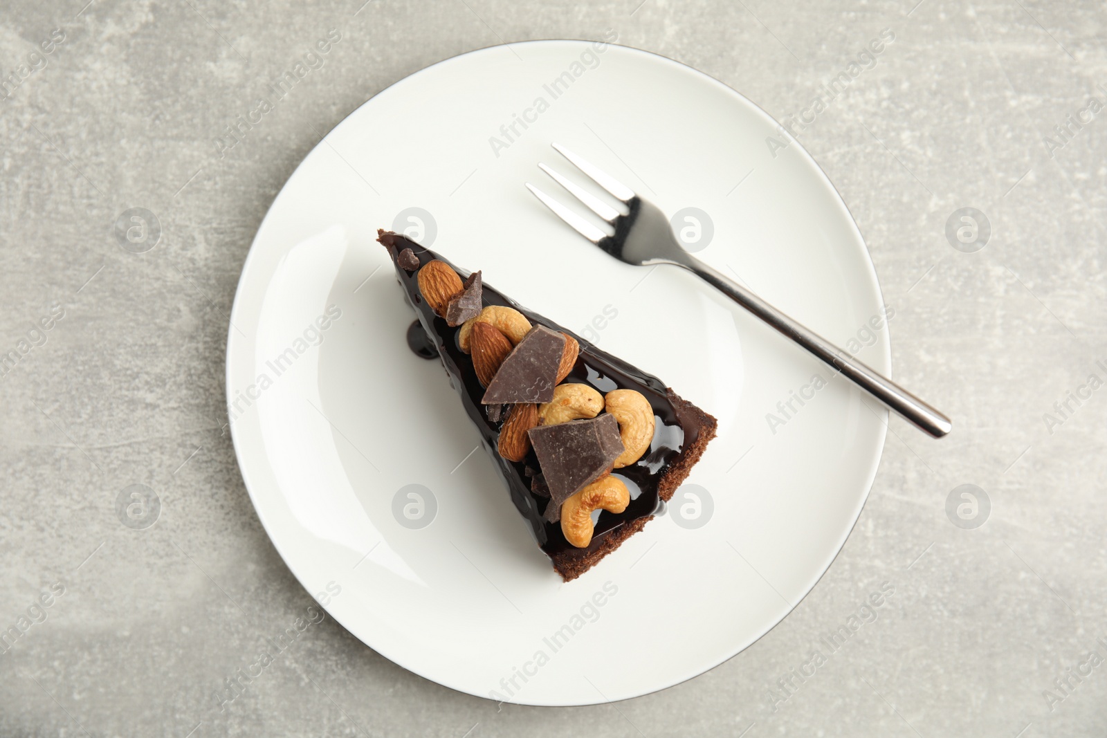 Photo of Piece of tasty homemade chocolate cake with nuts on grey table, top view