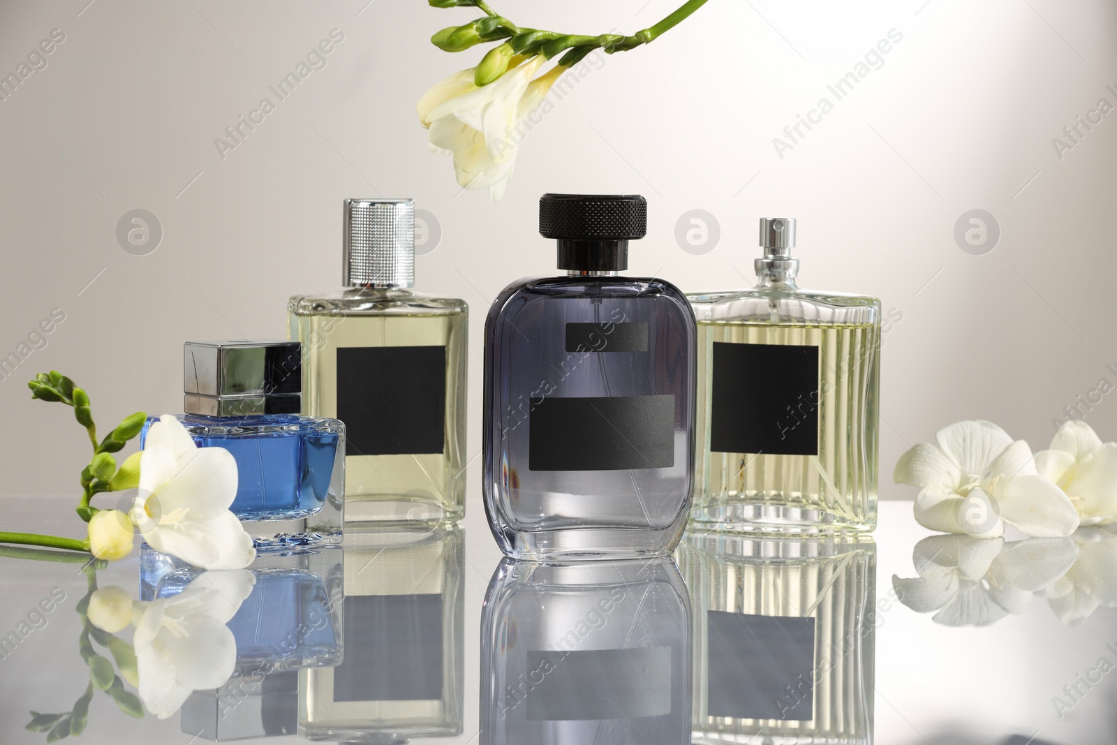 Photo of Luxury perfumes and freesia flowers on mirror surface against light grey background. Floral fragrance