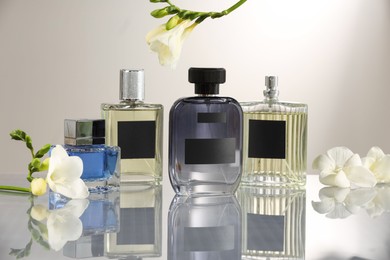 Photo of Luxury perfumes and freesia flowers on mirror surface against light grey background. Floral fragrance