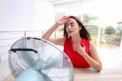 Photo of Woman with fan suffering from heat at workplace. Summer season