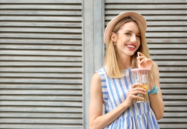 Young woman with cup of tasty lemonade near wooden wall