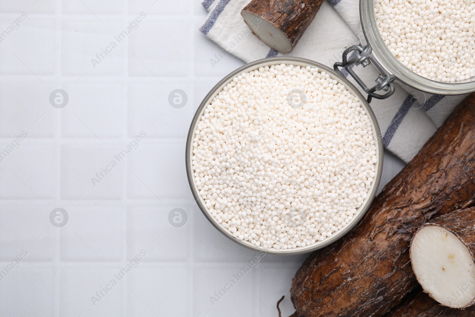 Photo of Tapioca pearls and cassava roots on white tiled table, flat lay. Space for text